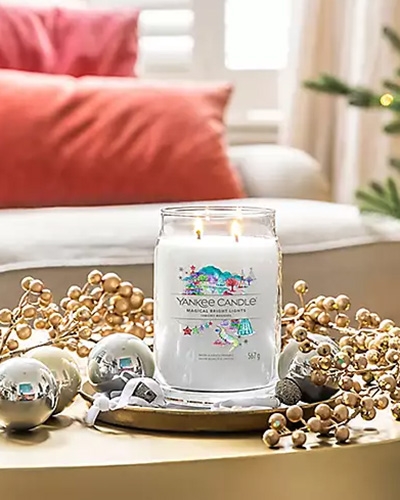 Bougie Yankee Candle allumée entourée de décorations de Noël dorées et argentées.